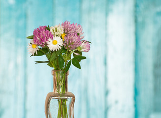 Wild flowers in vase on blue wood background