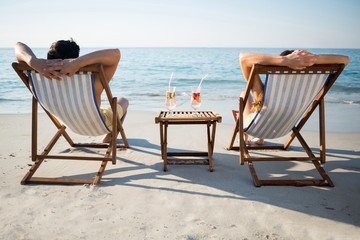 Couple relaxing on lounge chairs at beach