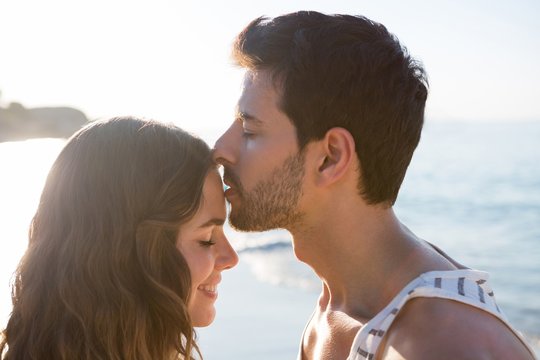 Young man kissing girlfriend forehead at beach