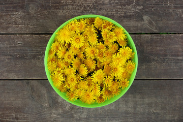 Green basket with yellow flowers of dandelions on the brown wooden background.
