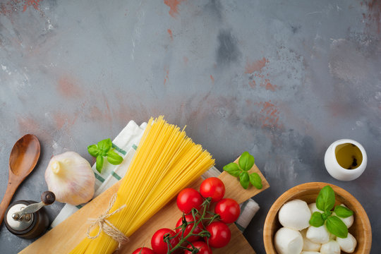 Raw ingredients for the preparation of Italian pasta, spaghetti,garlic, basil, mozzarella, pepper, cherry tomatoes and olive oil on gray concrete background. Selective focus.Top view. 