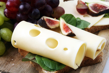 Bread with slices of cheese, some grapes and fig for lunch table. Sharing antipasti on party or summer picnic time