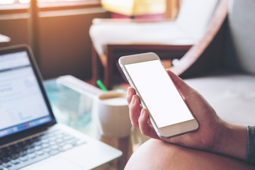 Mockup image of business woman holding mobile phone with blank white screen with latop on wooden table in cafe
