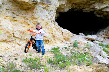 Obraz premium A little boy with a children's bicycle on the background of a rock and a ravine