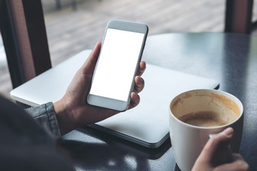 Mockup image of mobile phone with blank white screen with latop and coffee cup on wooden table in cafe