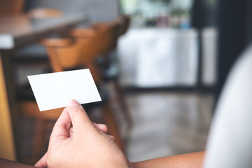 An image of a hand holding empty business card in modern cafe