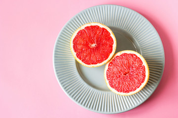 Beautiful appetizer fresh red grapefruit citrus fruit with half slice on blue plate and pink background close up top view natural vitamin C. Studio photography.