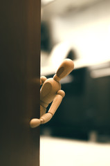 Wooden doll man peeking behind a door.