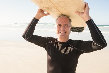 Portrait of smiling senior man carrying surfboard