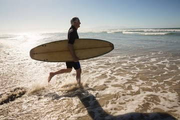 Side view of man carrying surfboard while walking on shore