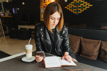 Business lady in cafe keeps the phone planning her week in note book.