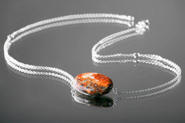 jasper jade pendant fiery red Jasper on a silver chain on the black glamorous backdrop of the mirror with the refraction and reflection
