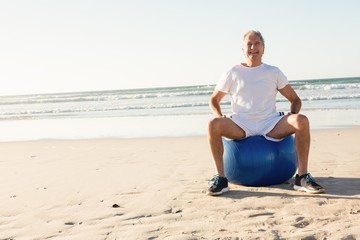Fototapeta na wymiar Portrait of smiling senior man sitting on ball against sea