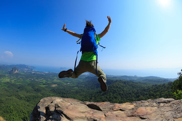 cheering successful young woman hiker jumping on mountain peak