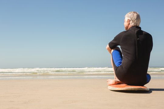 Senior man sitting on surfboard at beach on sunny day