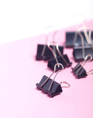 bunch of black paper clips on light pink and white background. 