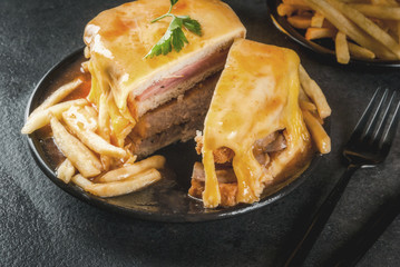 Traditional Portuguese snack food. Francesinha sandwich of bread, cheese, pork, ham, sausages, with tomato beer sauce and French fries. With a glass of beer and potatoes. On black table. Copy space