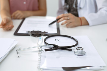Stethoscope, medical prescription form are lying against the background of a doctor and patient discussing health exam results 