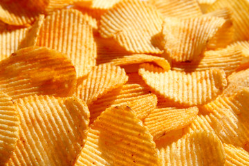 Background of golden wavy corrugated chips large slices with seasoning throughout the frame,...
