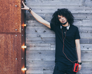 Young African American man with an afro hairstyle as DJ posing on wooden background. Headphones and...