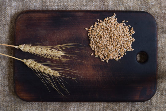 Wheat ears and grains on a kitchen board on a sacking background