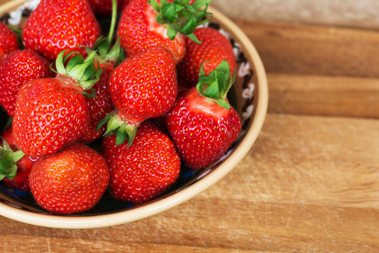 Fresh ripe strawberries in plate on a wooden background