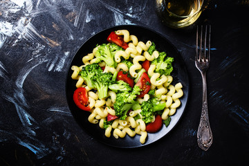 Cooked vegetarian pasta with broccoli and tomatoes, dark background, top view
