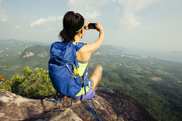 successful woman hiker taking photo with cellphone hiking on mountain peak