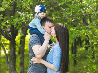 Obraz premium Family spending time together in the park in spring time. Mother, child and father in blooming garden.