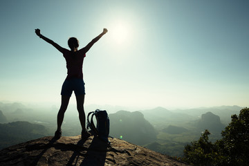 cheering successful woman hiker open arms on sunrise mountain top