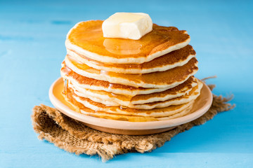Pancakes with butter and honey on blue wooden table.