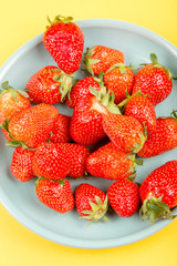 Fresh strawberry in a blue cup on a yellow background.