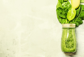 Spinach and banana green smoothies in a glass bottle, gray background, top view