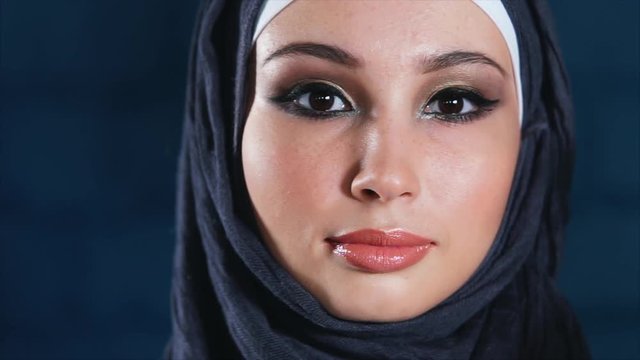 Slow motion close-up shot of final make-up touches for the young Muslim woman in black hijab looking to the camera
