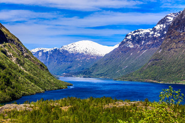 Naklejka na ściany i meble A beautiful spring day with snow on the mountain peaks, blue sky and green hills in Loen in Stryn.