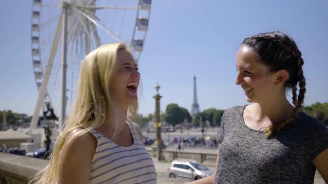 Portrait Of Two Young Women Laughing And Having Fun On Vacation In Paris, Ferris Wheel And Eiffel Tower Behind Them