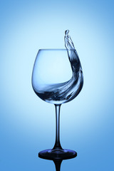 Splash of blue water in a glass on a dark blue background with reflection