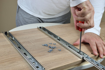 Man holding a screwdriver and installing drawer slides on an element of a chest of drawers