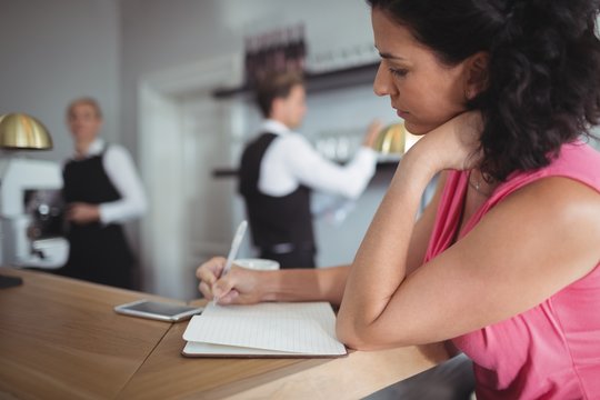Woman writing on a diary at bar counter