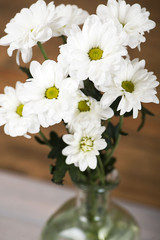 Close-up of flowers in a glass vase with water on wooden background. Daisy flower. Vertical shoot.