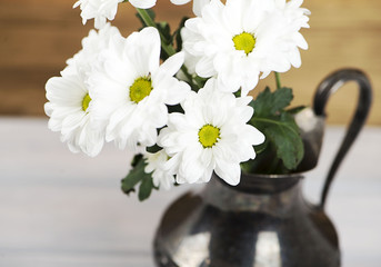 Close-up of flowers in iron vase on wooden table. Daisy flower.