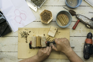 Close Up of a carpenter hands, he is building an insect shelter for wild bees on a workbench