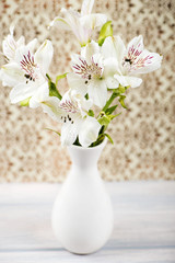 Flowers in white ceramic vase on decorated paper background. Lilies. Vertical shoot.