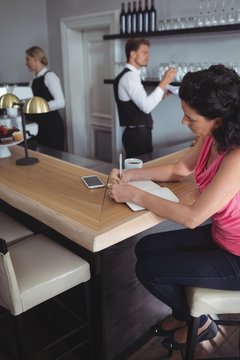 Woman writing on a diary at bar counter
