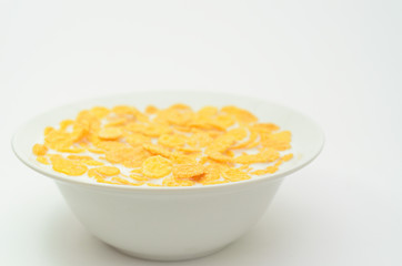 Cornflakes with milk on a spoon in a bowl on a light background.