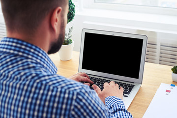 Male in fashionable blue checkered shirt working with laptop