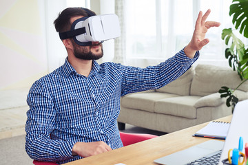 Appealing male in VR glasses orienting in space sitting at table