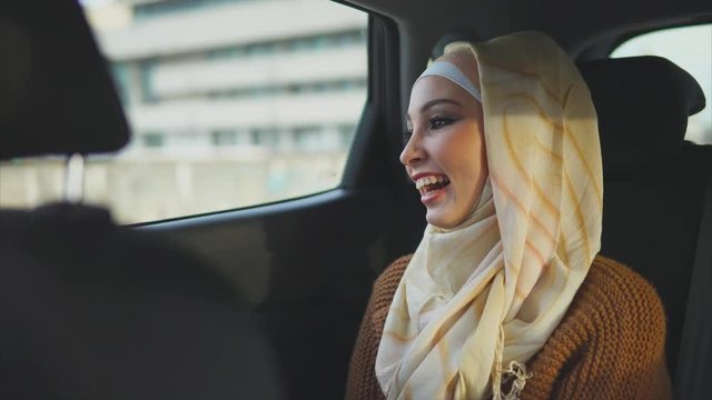 Young happy Middle Eastern woman traveling by taxi. She looking at the city through the window and enjoying the ride