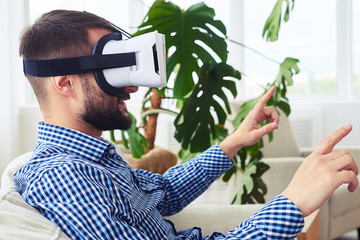Stylish gentleman in virtual reality goggles sitting on sofa