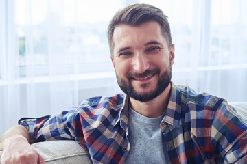 Smiling bearded mister leaning on back oh sofa and having rest